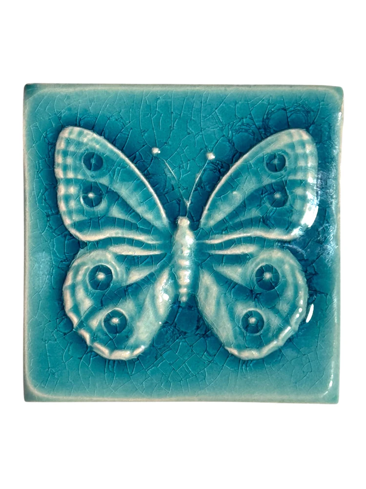 Türkise Relief-Fliese mit einem Schmetterling und Augenzeichnungen auf den Flügeln